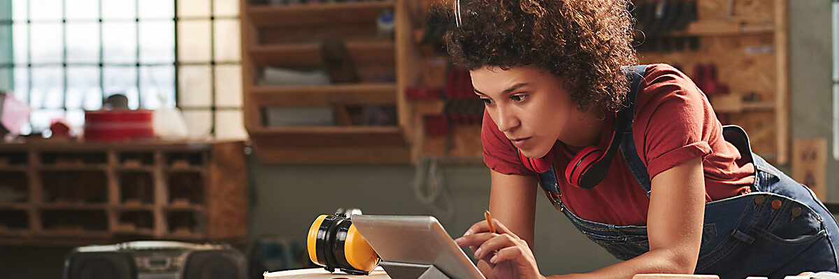 Young concentrated woman with curly hair reading instructions on digital tablet before working with wood Schlagwort(e): woman, female, young, attractive, curly, concentrated, digital, tablet, technology, internet, leaning, table, looking, reading, wifi, carpentry, joinery, timber, wood, wooden, plank, tool, skill, manual, equipment, professional, craft, craftsman, handyman, occupation, working, woodworking, workshop
