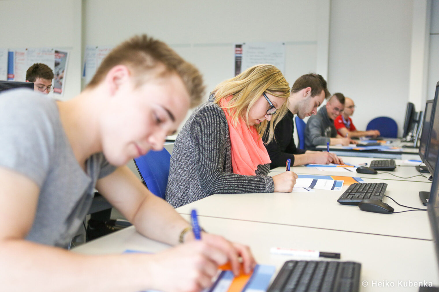 Unterrichtssituation - junge Teilnehmende schreiben auf Arbeitsblätter Unterrichtssituation - junge Teilnehmende schreiben auf Arbeitsblättern, während sie vor Computern sitzen