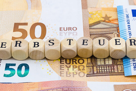 Geldscheine und darüber liegen Holzwürfel mit den Buchstaben für das Wort Erbsteuer