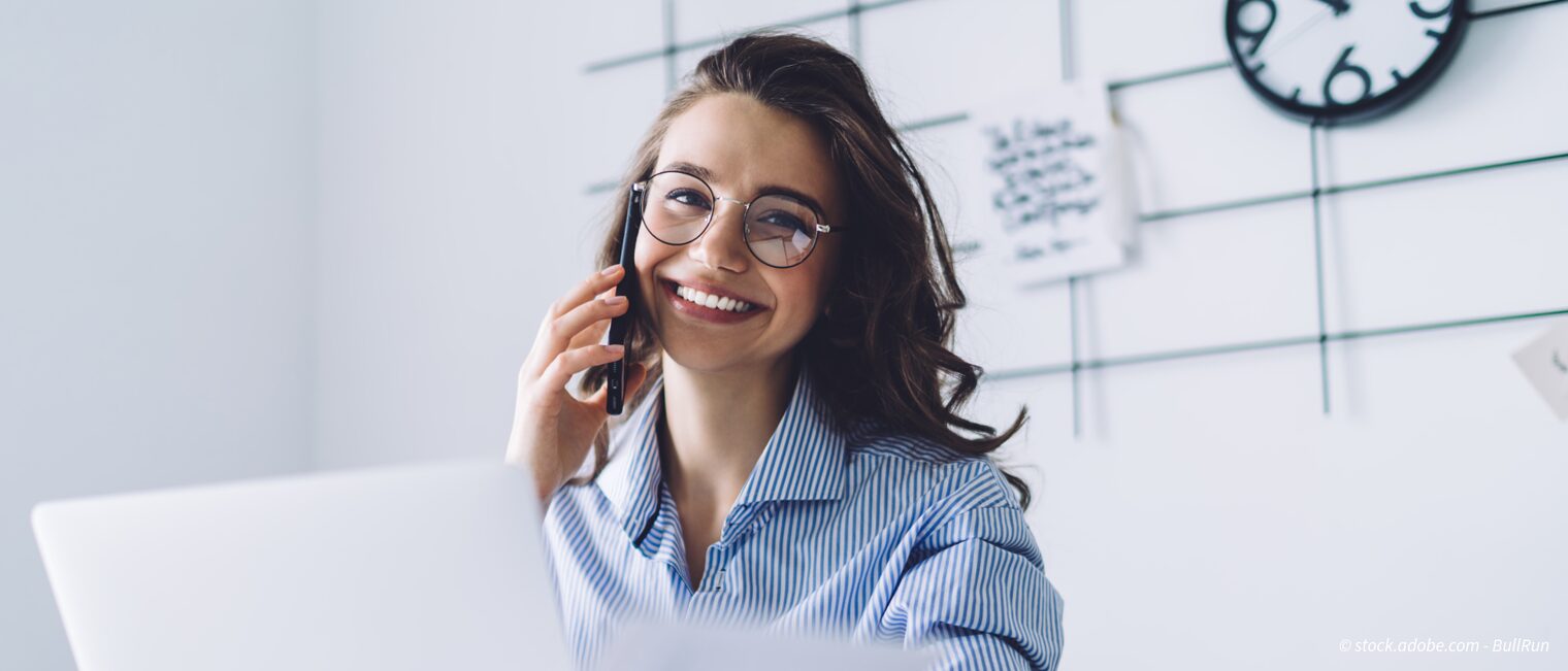 Junge Frau lächelt in die Kamera und telefoniert mit dem Handy Stellenausschreibung: QualiTec GmbH sucht Sachbearbeiter Entgeltabrechnung (w/m/d). 