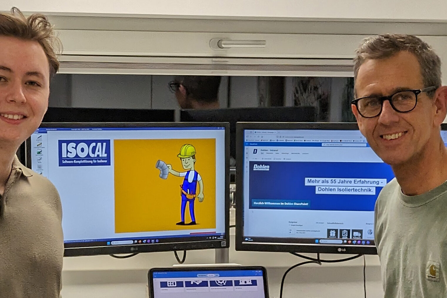 Udo und Bastian Dohlen der Firma Dohlen Isoliertechnik stehen vor einem Schreibtisch mit mehreren Bildschirmen und einem Laptop. Sie sprechen über Digitalisierung
