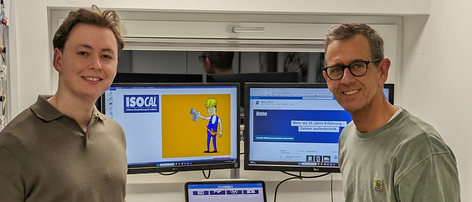 Udo und Bastian Dohlen der Firma Dohlen Isoliertechnik stehen vor einem Schreibtisch mit mehreren Bildschirmen und einem Laptop. Sie sprechen über Digitalisierung