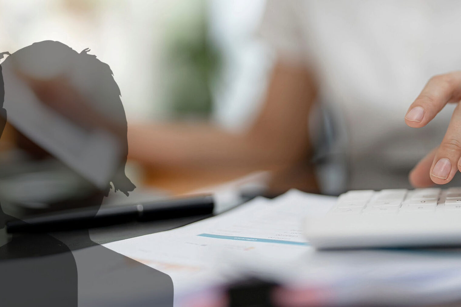 Bild zeigt eine Frau, die im Büro arbeitet und Unterlagen, einen Rechner und ein Laptop bedient.