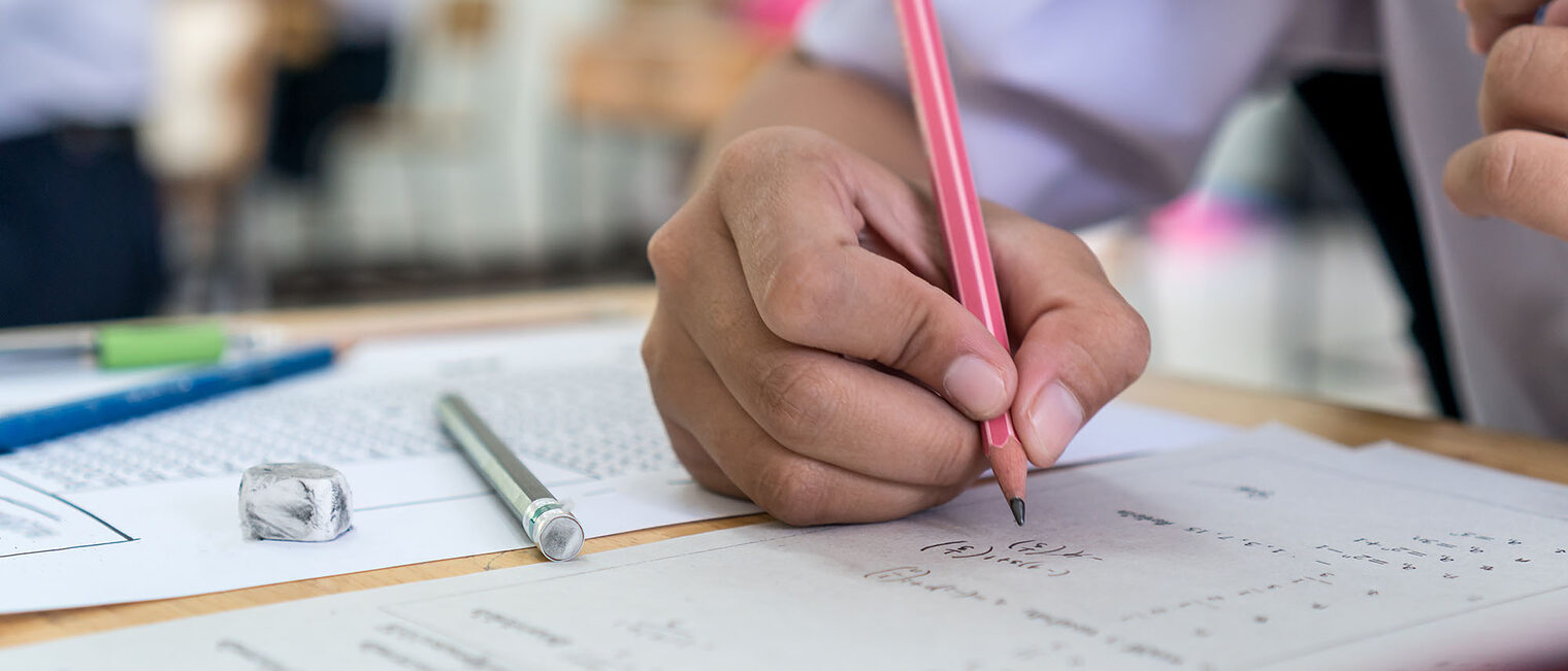 Das Bild zeigt eine Situation in der schriftlichen Prüfung. Person löst handschriftlich Aufgaben auf einem Blatt.